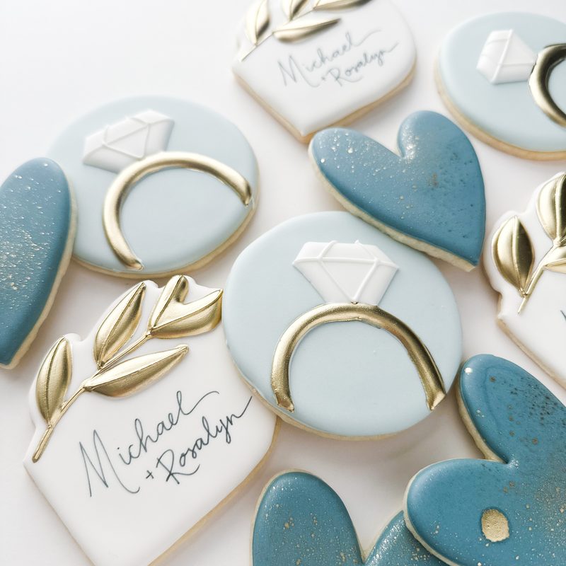 A wedding set in dusty blue and gold: diamond rings, hearts, olive branches and hand-lettered names.