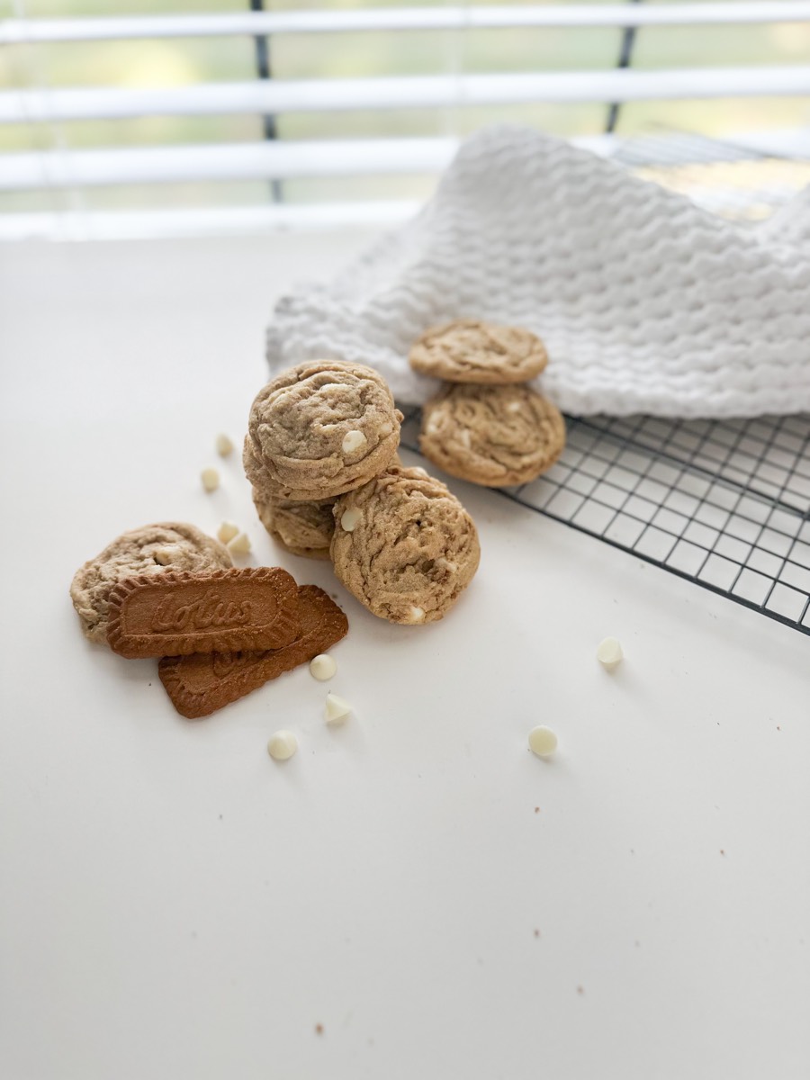White chip cookies stacked beside Biscoff biscuits and a white waffle towel.