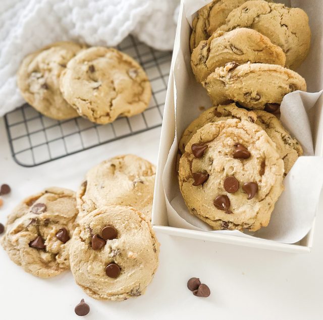 Chocolate chip cookies cooling on a wire rack and packed into a white box.