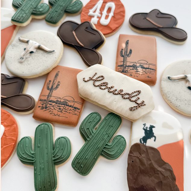 A western-themed set: cactus cookies, cowboy hats, a steer skull and a hand-lettered howdy plaque.
