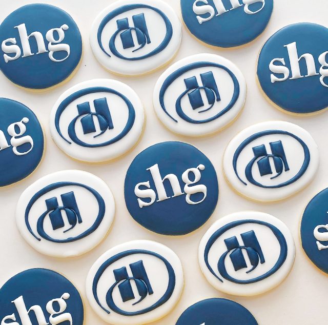 Rows of round cookies iced in navy and white with a corporate monogram and wordmark.
